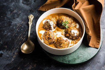 Malai Kofta is a Mughlai Speciality dish served in a bowl or pan over moody background. selective focus