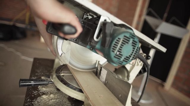 View of wooden plank being cut with new modern circular saw operated by man's hand in workhouse in daylight room.