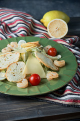 Fresh caesar salad with shrimps in a green plate on a light wooden table