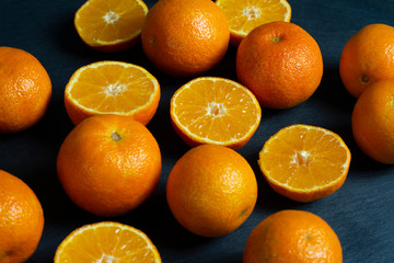 A lot of sliced and whole mandarins on a black background.