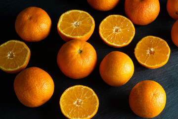 A lot of sliced and whole mandarins on a black background.