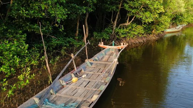 Low aerial drone view flying over a parked wooden fishing boat in a mangrove forest estuary in coastal Southeast Asia. Mangrove roots and second boat can be seen in background
