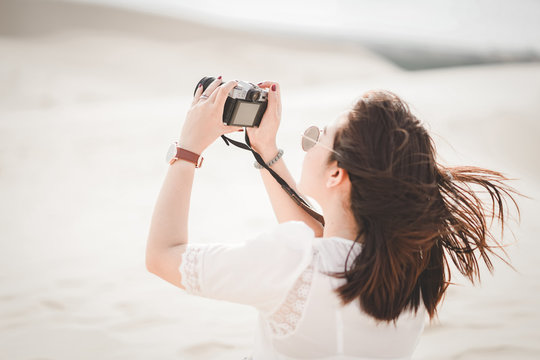 Traveling and photography. Young woman with camera taking photo at White Sand Dunes, Vietnam.