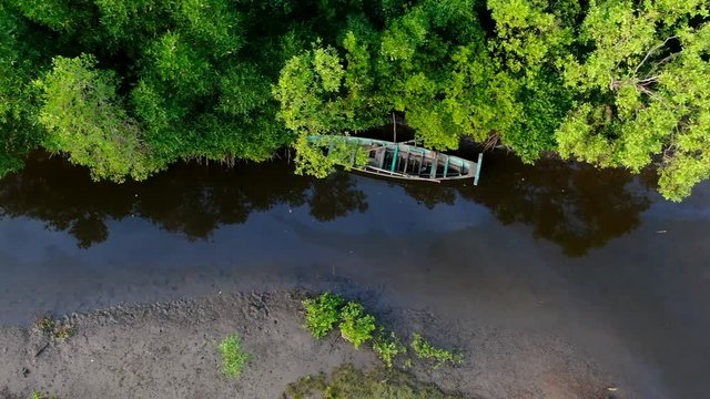 Aerial drone view flying along a mangrove forest estuary leading from the sea towards the interior of a coastline in Southeast Asia. A small boat is seen below, with camera ascending 
