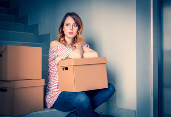 young redhead woman with moving boxes sitting on stairs in house. European ethnicity