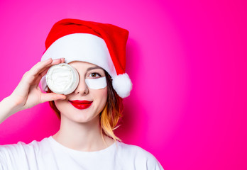 Fototapeta na wymiar Woman using eye patch for her eyes in Santa Claus hat with cream on pink background isolated. Portrait of natural and true female as usually they are looks like