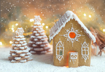 Gingerbread house and Christmas trees on a luminous background. Bokeh effect.