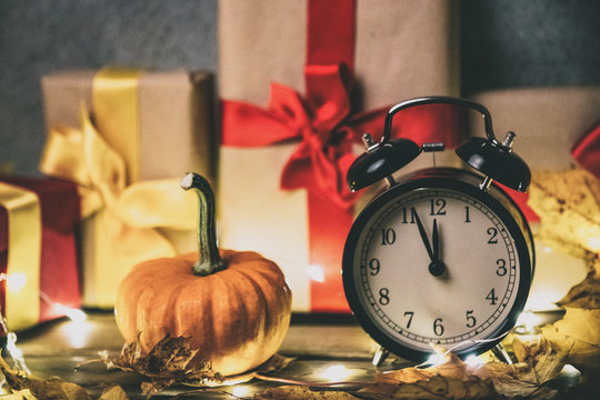 Retro alarm clock with leaves and pumpkin with Halloween gift box on background. Autumn season image composition