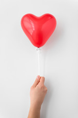 valentines day and romantic concept - close up of hand holding red heart shaped balloon on stick...