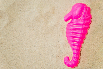 Fototapeta na wymiar toys, childhood and vacation concept - close up of pink sea horse mold on summer beach sand