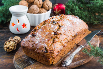 Christmas carrot and chocolate cake on cutting board on wooden rustic table decorated with candle and green fir-tree brunches.