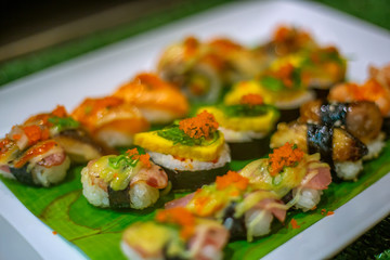The row of rolled sushi with shrimp orange eggs and sea weed on the white ceramic tray in the incandescent light of restaurant.