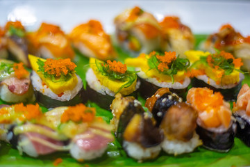 The row of rolled sushi with shrimp orange eggs and sea weed on the white ceramic tray in the incandescent light of restaurant.