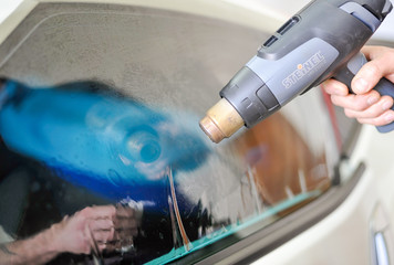 Man shaping the window tinting film with a heat gun. Professional window tinting services.