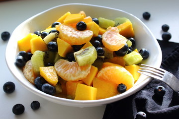 Bowl of fruits: mandarin, mango, blueberries and kiwi.