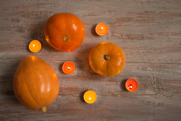 Orange pumkins with colorful candles on the wooden boards.