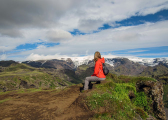 Active young hiker woman small backpack sitting enjoying volcano landscape with glacier mountains green valley and snow Thorsmork Iceland