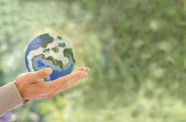 Human holding Earth in hands against green spring background and sun ray. Ecology concept,