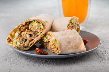 Close-up of Doner kebab rolls on a plate with dried tomatoes and orange juice.