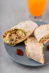 Close-up of Doner kebab rolls on a plate with dried tomatoes and orange juice.