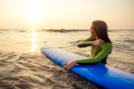 Beautiful woman in a diving suit for swimming surfing in the Indian Ocean on the background sunset sky and waves.professional surfer girl in a wetsuit doing sports at sea.extreme, adrenaline and youth