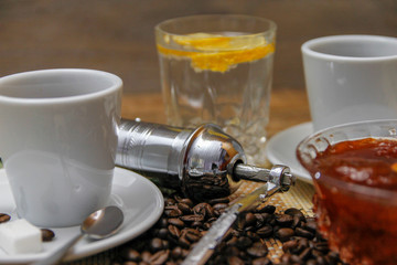 Coffee on wooden table and old manual coffee grinder. Mineral water and traditional plum jam with lemon. coffee beans spilled on the table.