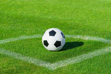 A classic soccer ball lies on the bright green grass on the football field in the designated area of the penalty area at a sports stadium close-up in a large sports center for football players