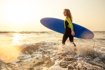 Young freelancing woman in a wetsuit swimming over surfboard in the water at beach.surfer girl relaxing in paradise island sunset romance and freelance freedom in the Indian Ocean.