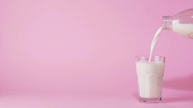 Cinemagraph, hand pouring milk into glass on pink background.