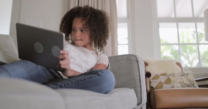 African American girl playing games on digital tablet at home on sofa