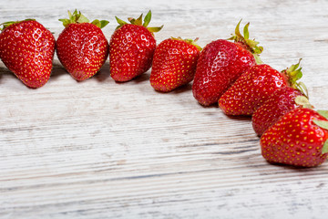 An arc of fresh ripe red strawberries lies on a light textured wooden table. Close-up. Copyspace