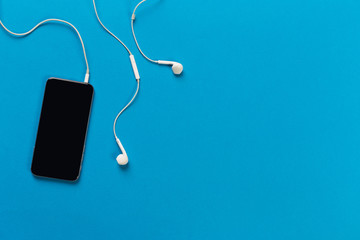 Mobile phone with white earphones on colour backgroung, top view