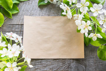 Spring blossoming branches with craft paper sheet for text on a wooden background. Space for text.