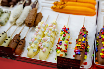 Bananas, strawberries, raspberries and apples covered with chocolate, marshmellows and various glazes for sale in a shop window. Selling sweets at the Christmas market. In German price for fruits.