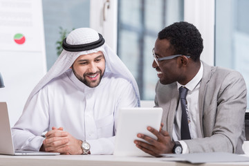 Fototapeta na wymiar Multiethnic partners looking on digital tablet and smiling in modern office