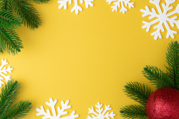 Christmas background with fir branches, snowflake and new year toy red ball or bauble flat lay on yellow pastel  background. Top view. Minimal concept