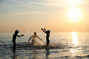 Fototapeta premium Children's Silhouette - Happy Brothers Having Fun, Splashing Each Other And Fooling Around In The Sea At Beautiful Sunset
