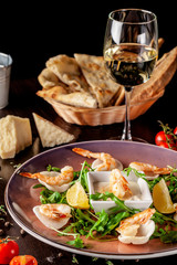 The concept of Italian cuisine. Tiger prawns on rice chips in a creamy sauce. Arugula salad and lemon. On the table is a glass of red wine. beautiful serving in the restaurant