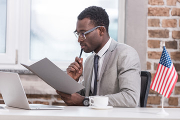 African american businessman holding folder and sitting at office desk