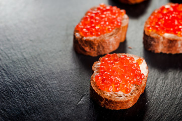Red caviar on bread on slate background.