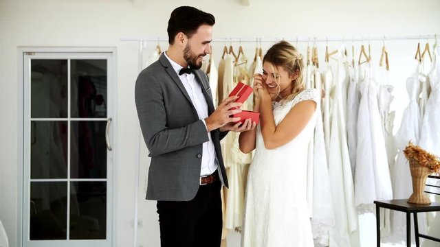Romantic wedding couple in expensive dress shop. White man and woman in bride dress, man giving present to surprise his woman. Romantic young couple concept.