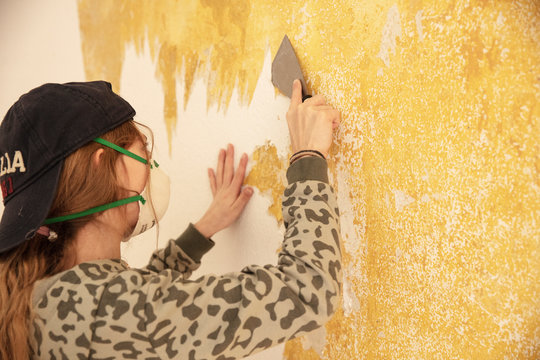 Young girl stripping wallpaper from old wall. Munich, Germany