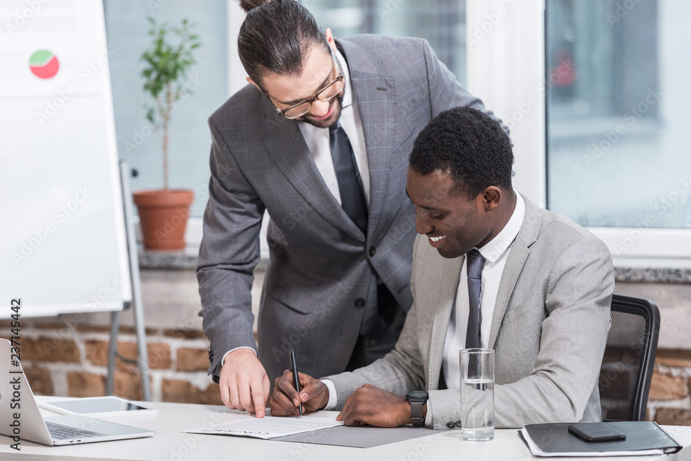 Wall mural multiethnic businessmen smiling and signing document in modern office