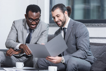 smiling multiethnic businessmen reading document in office