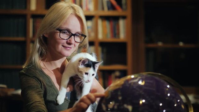 Woman with a cat in hand looks at the globe