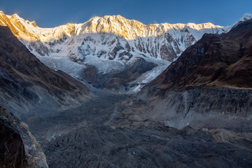 Horizontal photo of Annapurna 1 and its glacier morraine during sunrise (golden hour) against blue sky, Himalayas
