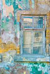 Colored photo of an old window frame with glass and metal bars inside the old dilapidated wall