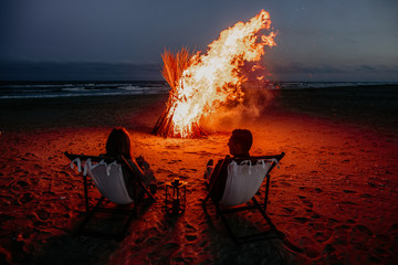 Romantic mature couples watch the sea in front of campfire at night