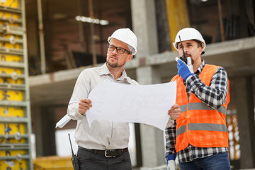 Male architect and developer with walkie talkie and blueprints at construction site