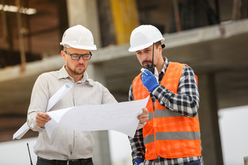 Male architect and developer with walkie talkie and blueprints at construction site
